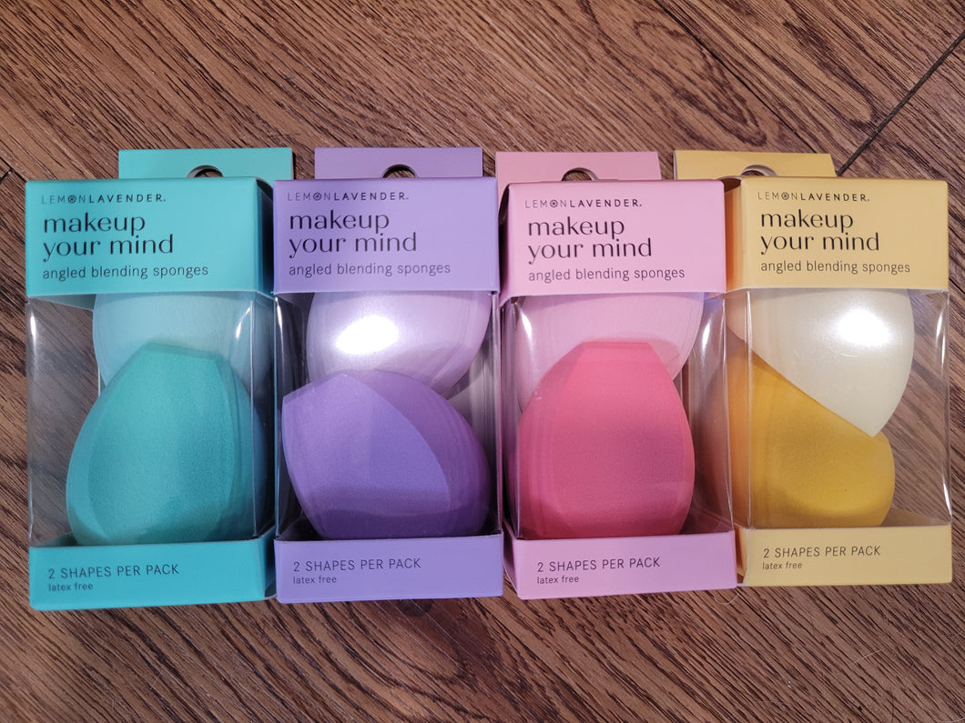 Four packages of 'makeup your mind' angled blending sponges in different colors on a wooden surface.